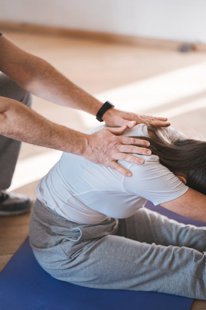 Person stretching on a yoga mat with assistance indoors. Exercise and wellness concept.
